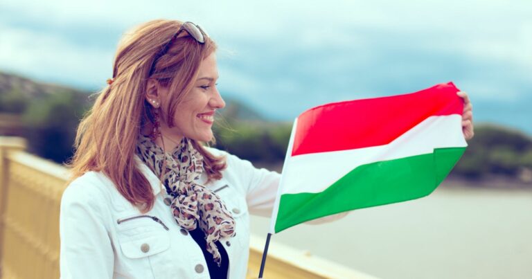 Fiatal nő hídon áll, kezében lobog egy kisméretű magyar zászló.