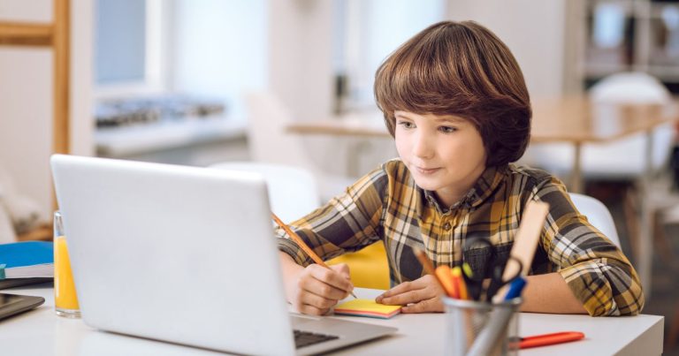 A képen egy laptop előtt tanuló kisfiú látható.